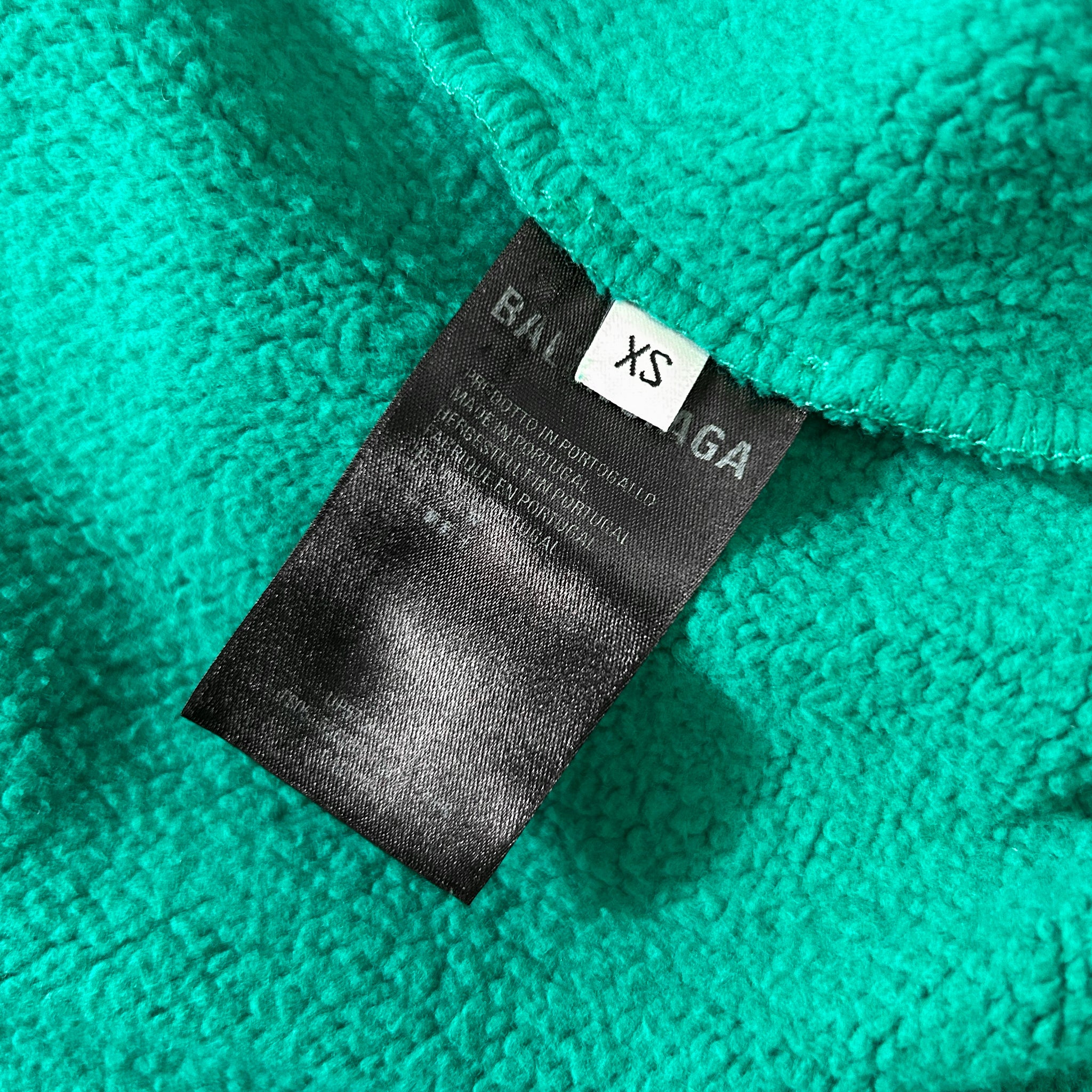 A close-up image of a green fabric with a black label attached to it, displaying text and a small white label.
