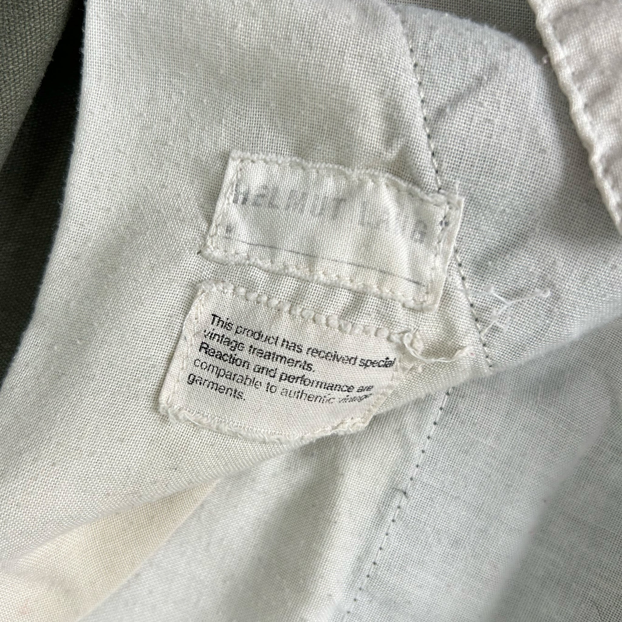 a close-up view of a white fabric, possibly a piece of clothing or a textile, with a small label attached to it. The label appears to contain text, but it is not clear enough to transcribe accurately.