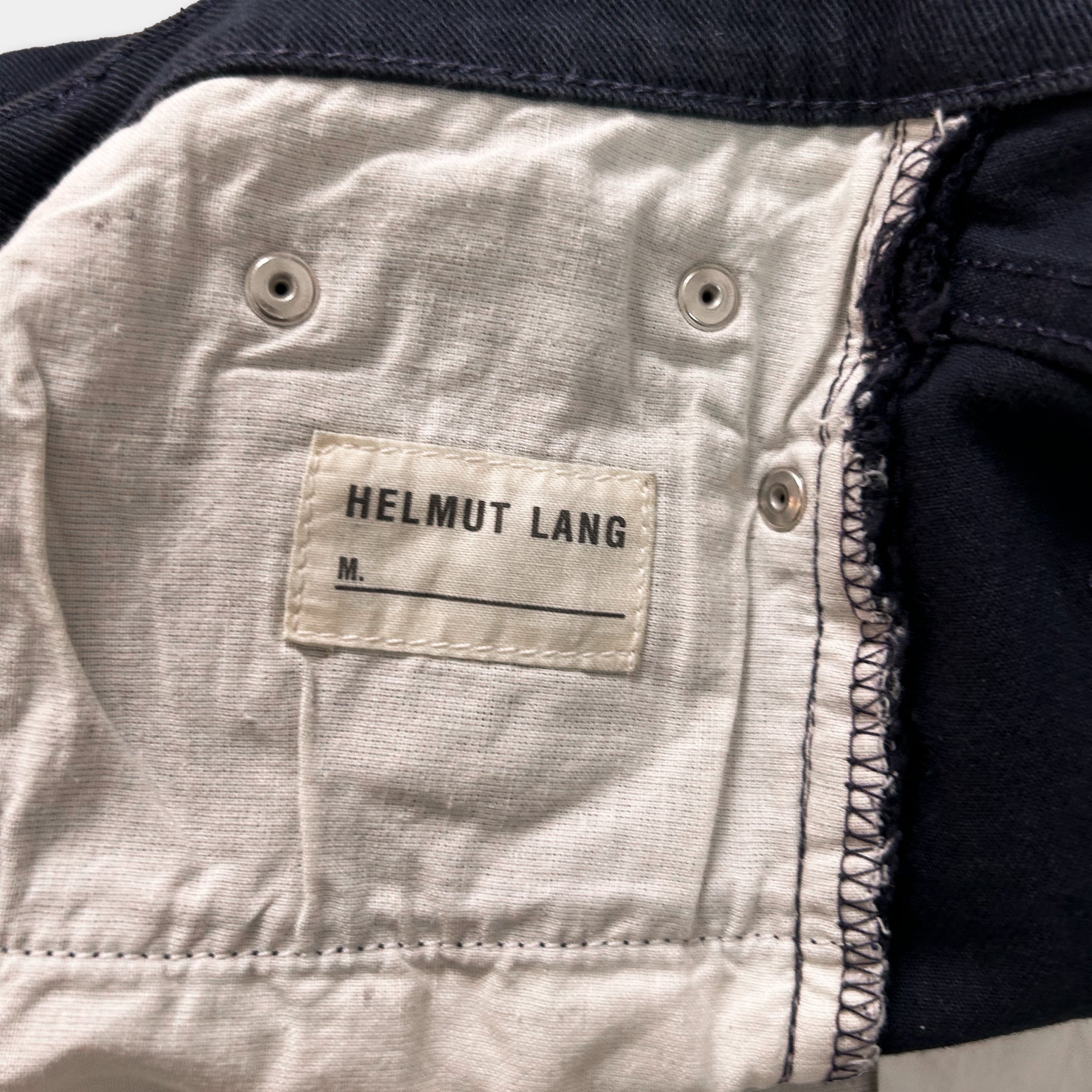 A close-up view of a fabric label on a pair of navy blue jeans, with the brand name "Helmut Lang" printed on it.