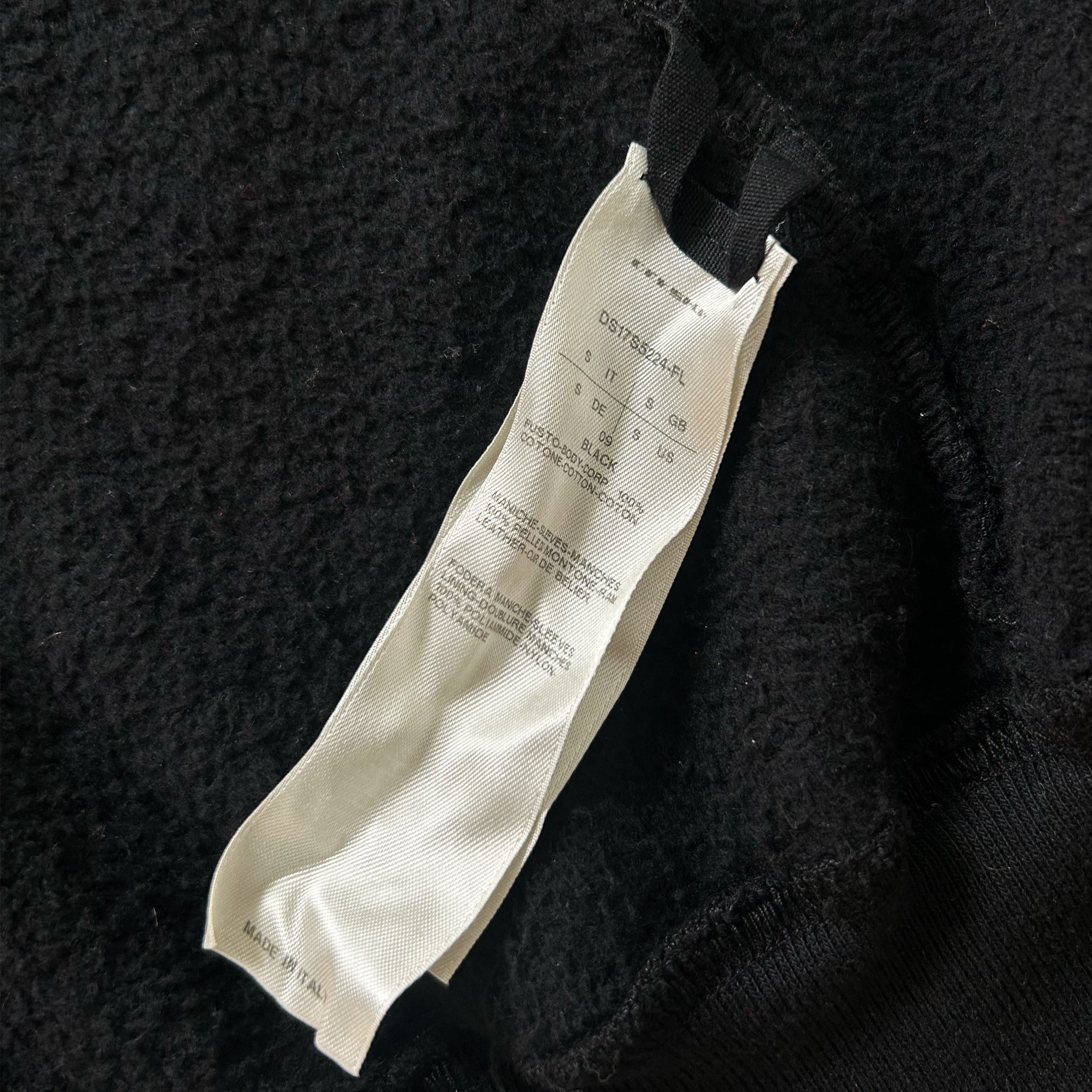 a close-up view of a black fabric with a white label attached to it. The label appears to contain text and possibly a barcode or other information, but it is not possible to transcribe the text accurately without more context.