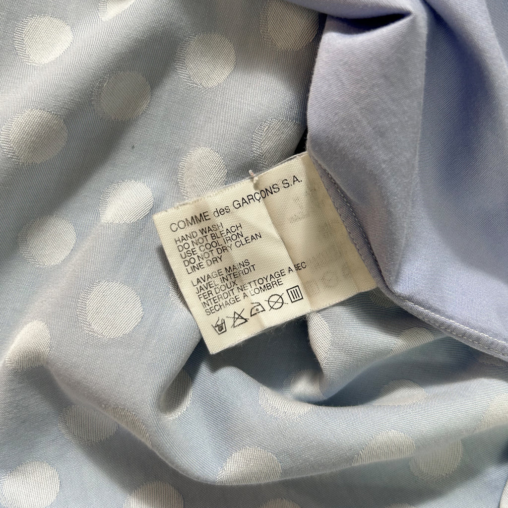 a close-up view of a fabric with a white polka dot pattern. There is a label attached to the fabric, which contains text and symbols.
