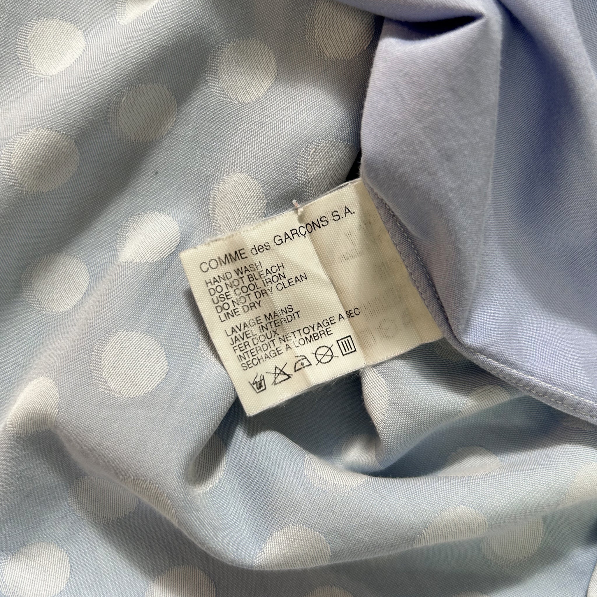 a close-up view of a fabric with a white polka dot pattern. There is a label attached to the fabric, which contains text and symbols.