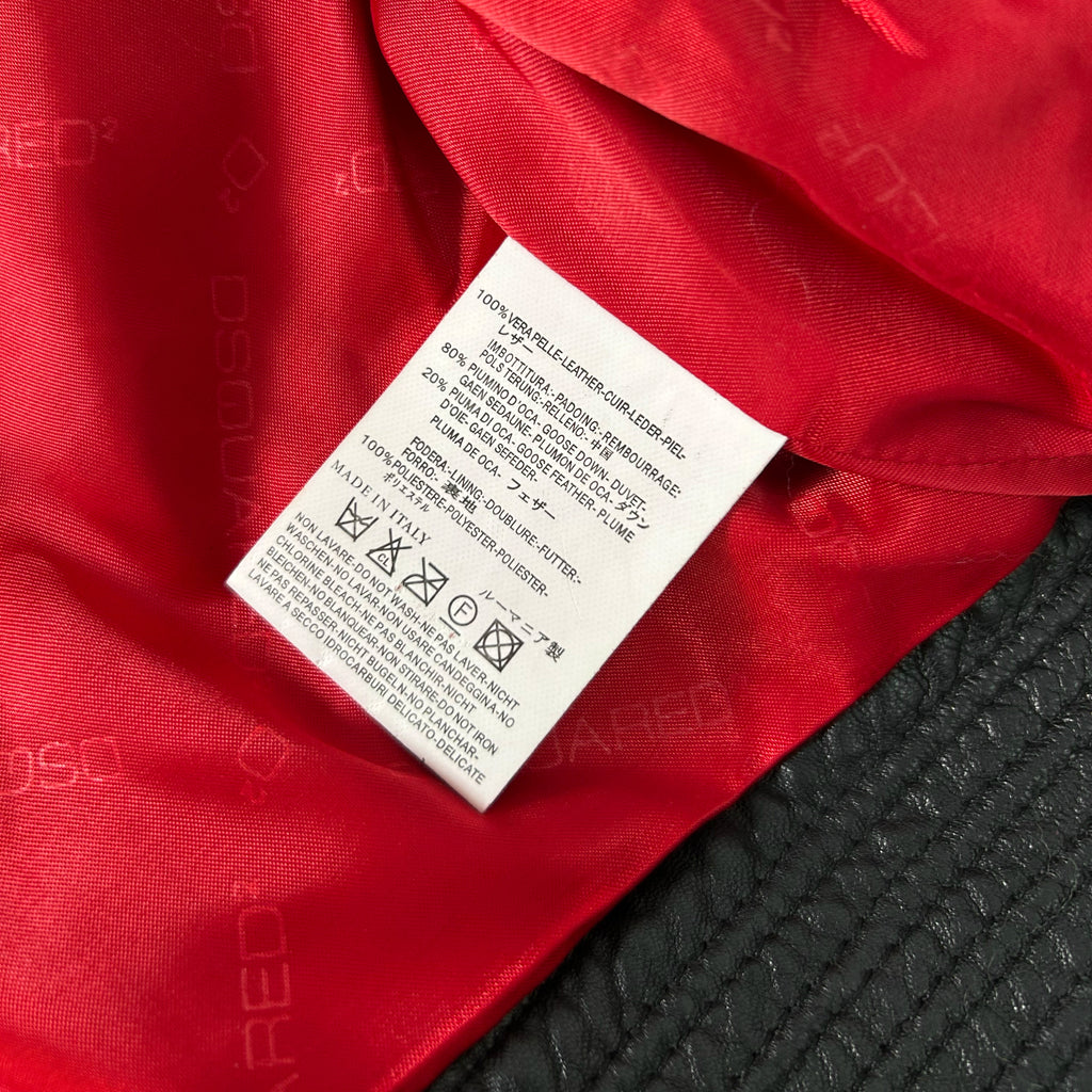 a close-up view of a red fabric, possibly a jacket or sweater, with a white label attached to it. The label appears to contain text and symbols, likely providing information about the product or its care instructions.