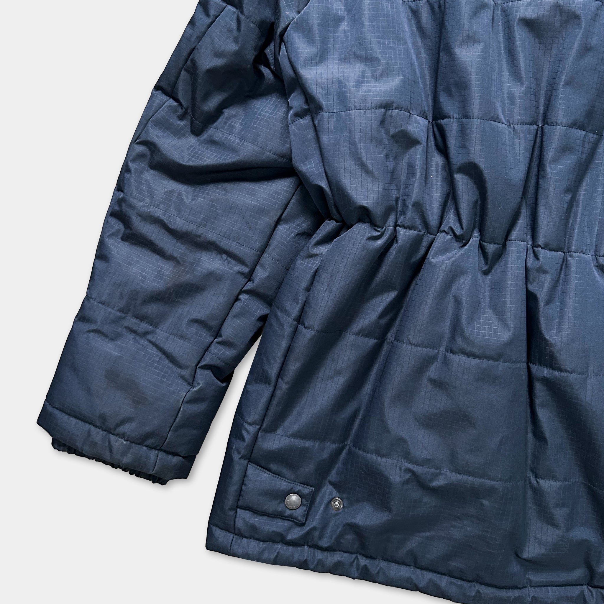 A close-up view of a navy blue puffer jacket with a textured fabric and a button on the back.