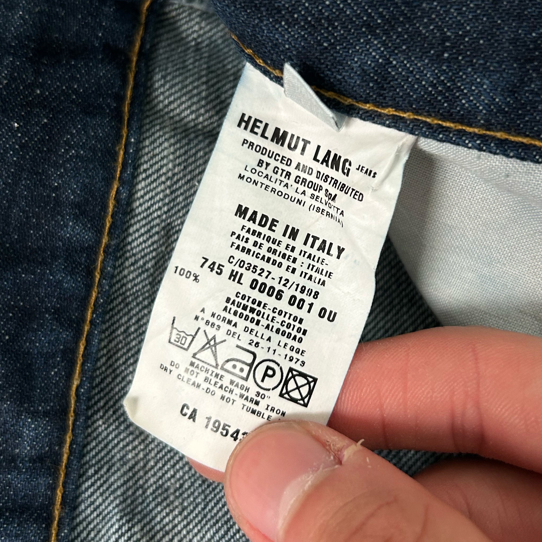 A close-up of a person's hand holding a denim fabric label with text and symbols.