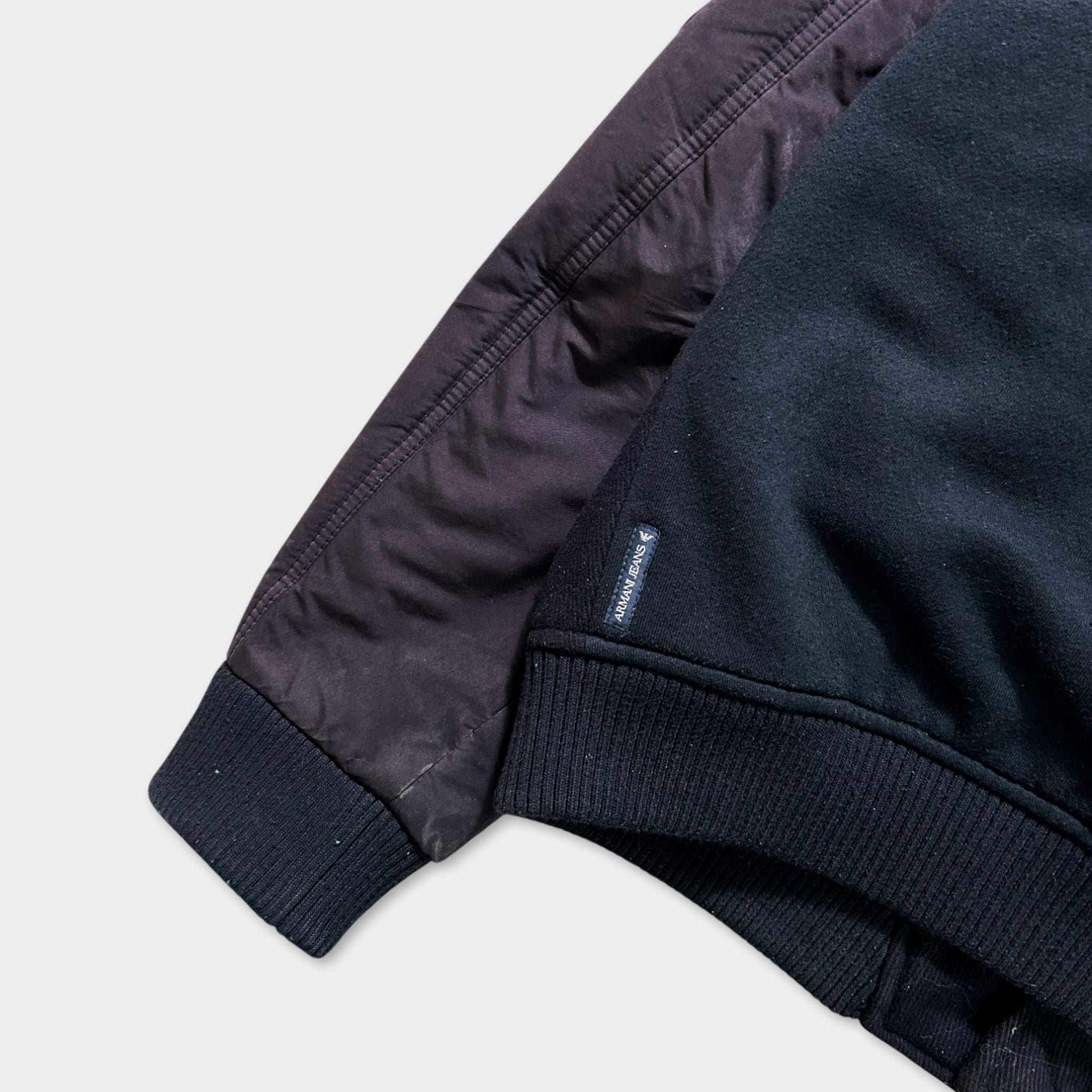 A dark-colored jacket with a dark sleeve and a small blue label on the right side.