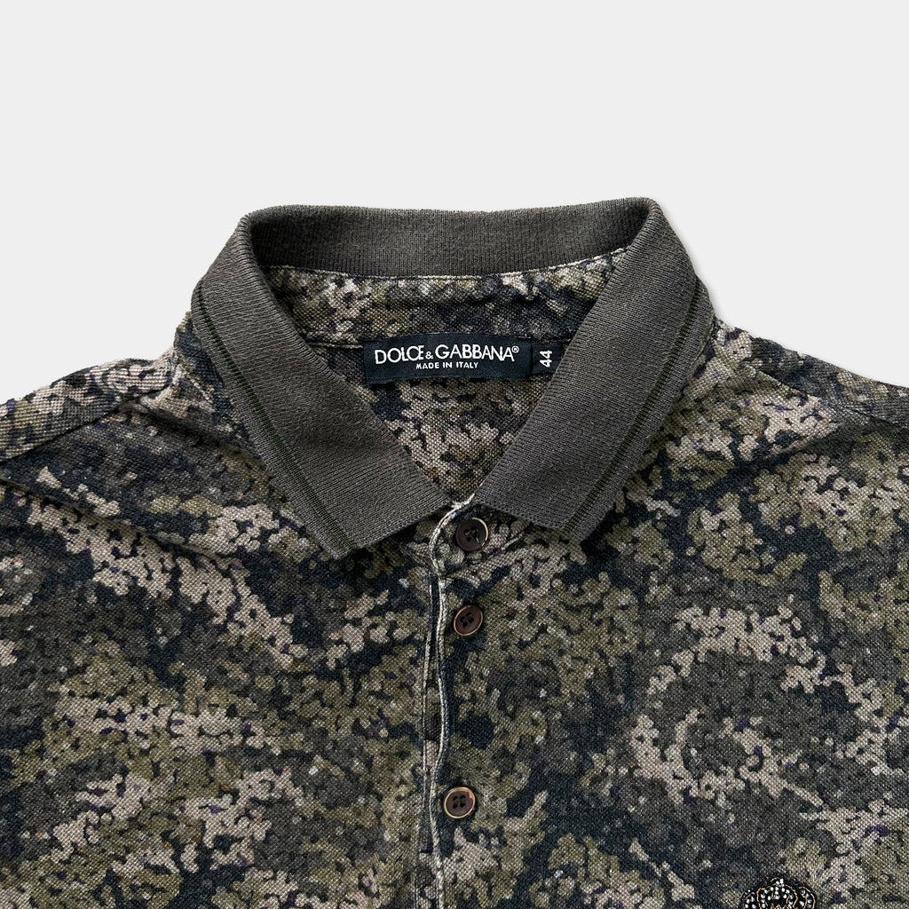 A close-up view of a polo shirt with a camouflage pattern, featuring a collar and three buttons.