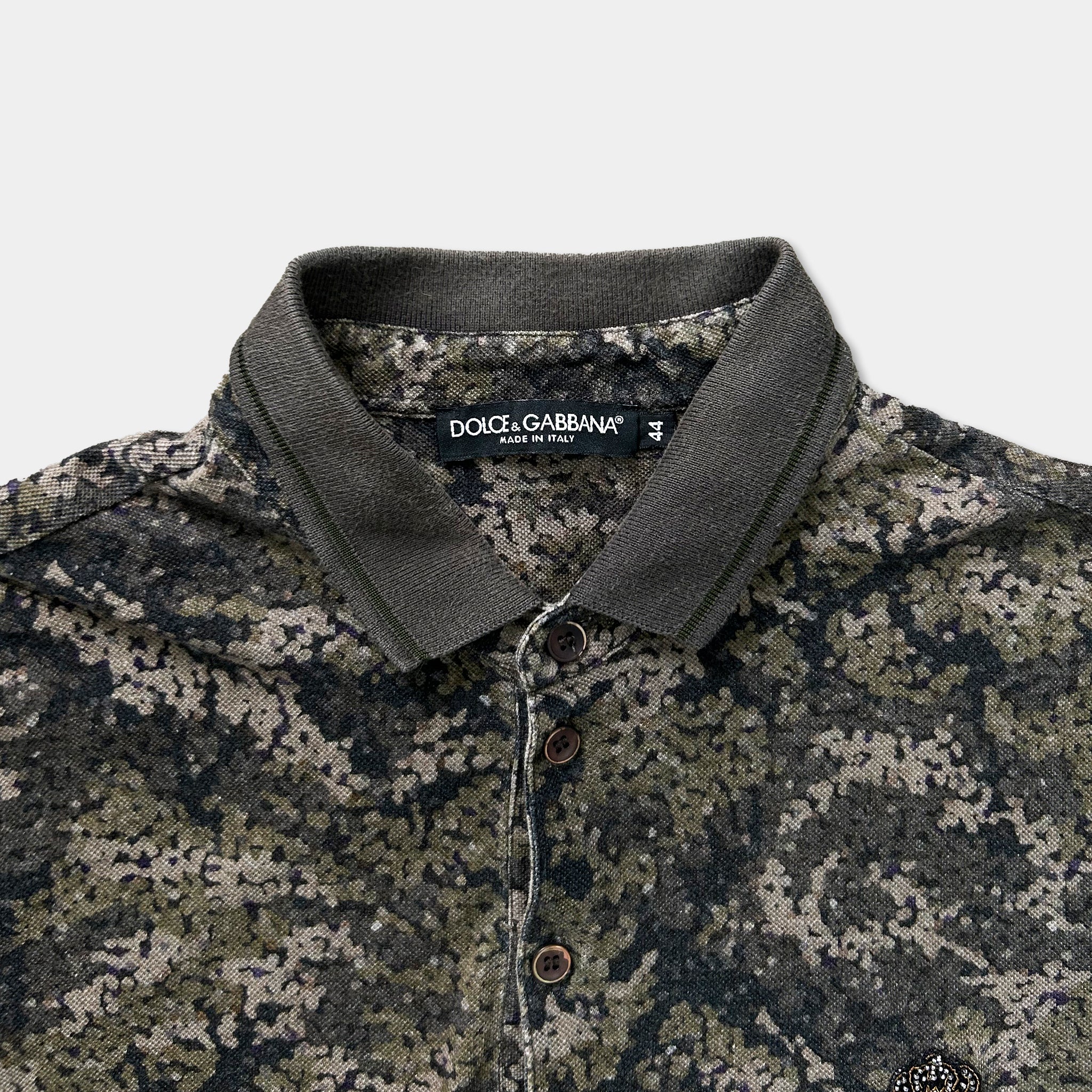 A close-up view of a polo shirt with a camouflage pattern, featuring a collar and three buttons.