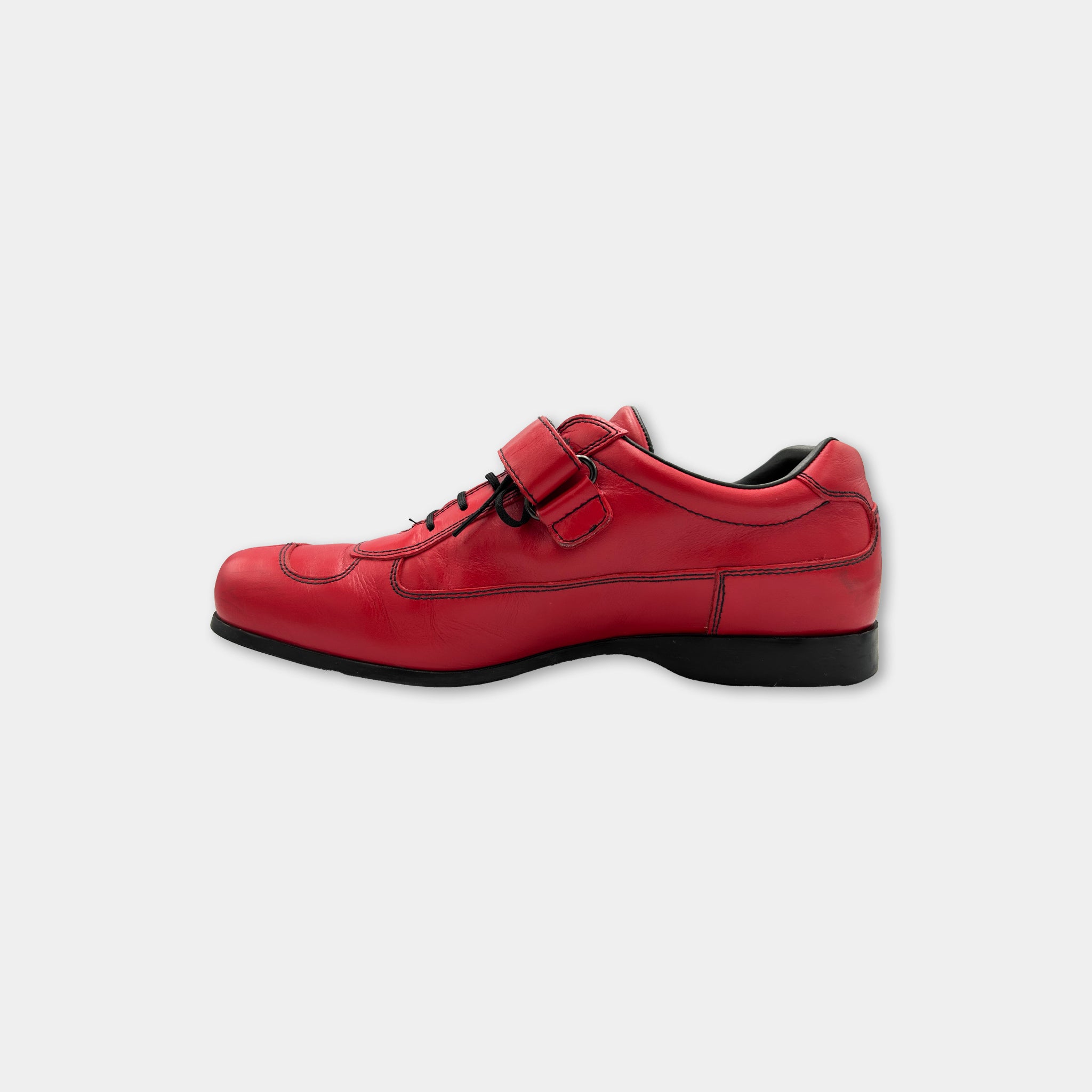 A red leather shoe with a black sole and laces is shown against a white background.