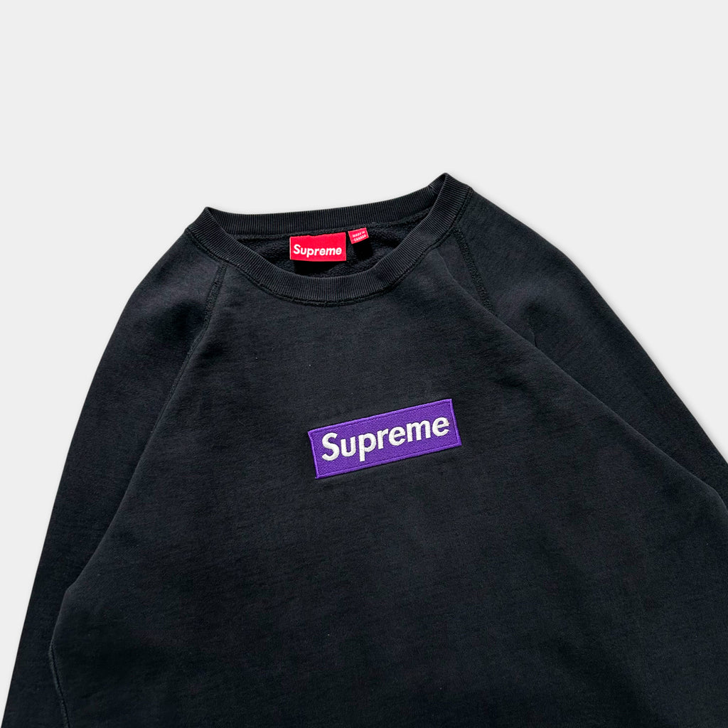 A black sweatshirt with a purple Supreme logo on the front.