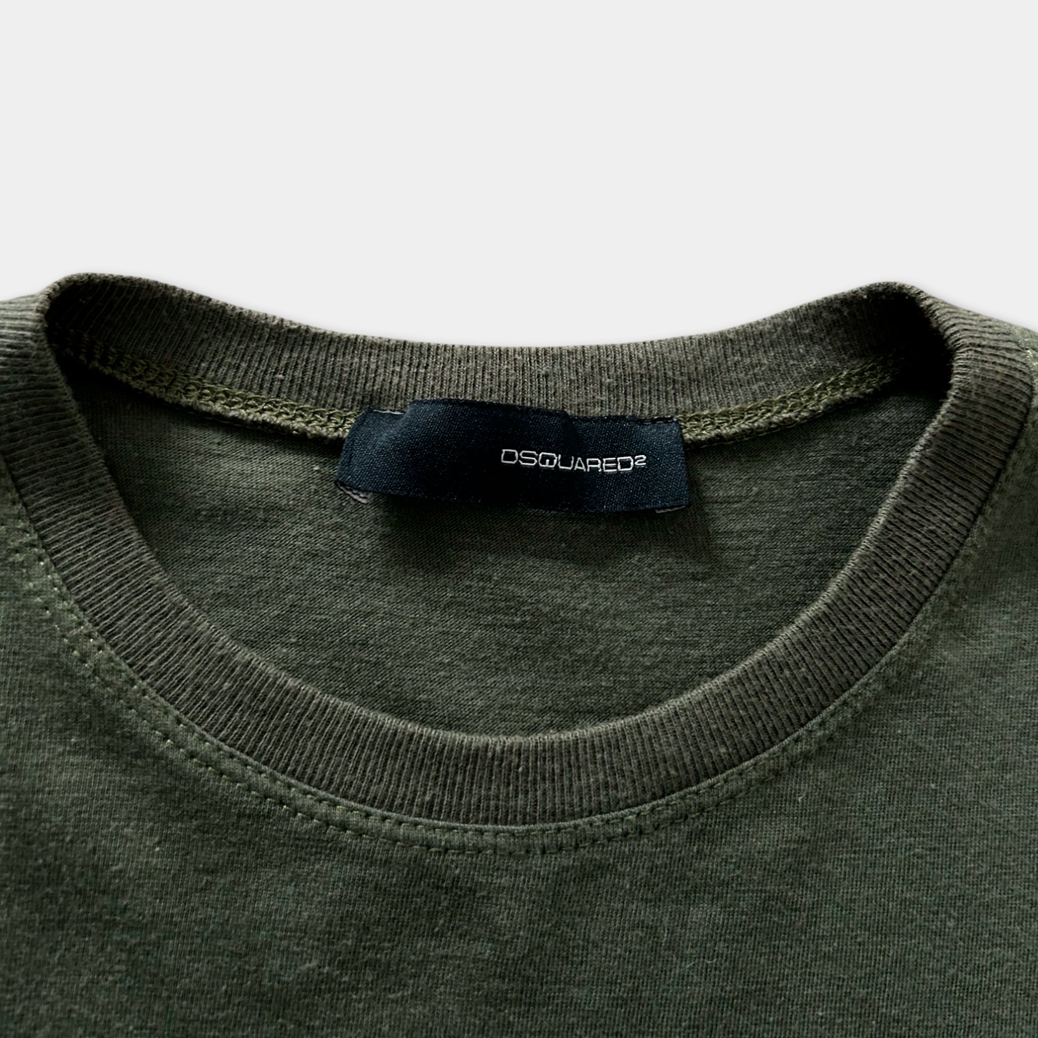 A close-up view of a dark green t-shirt with a black label that reads "DSQUARED".