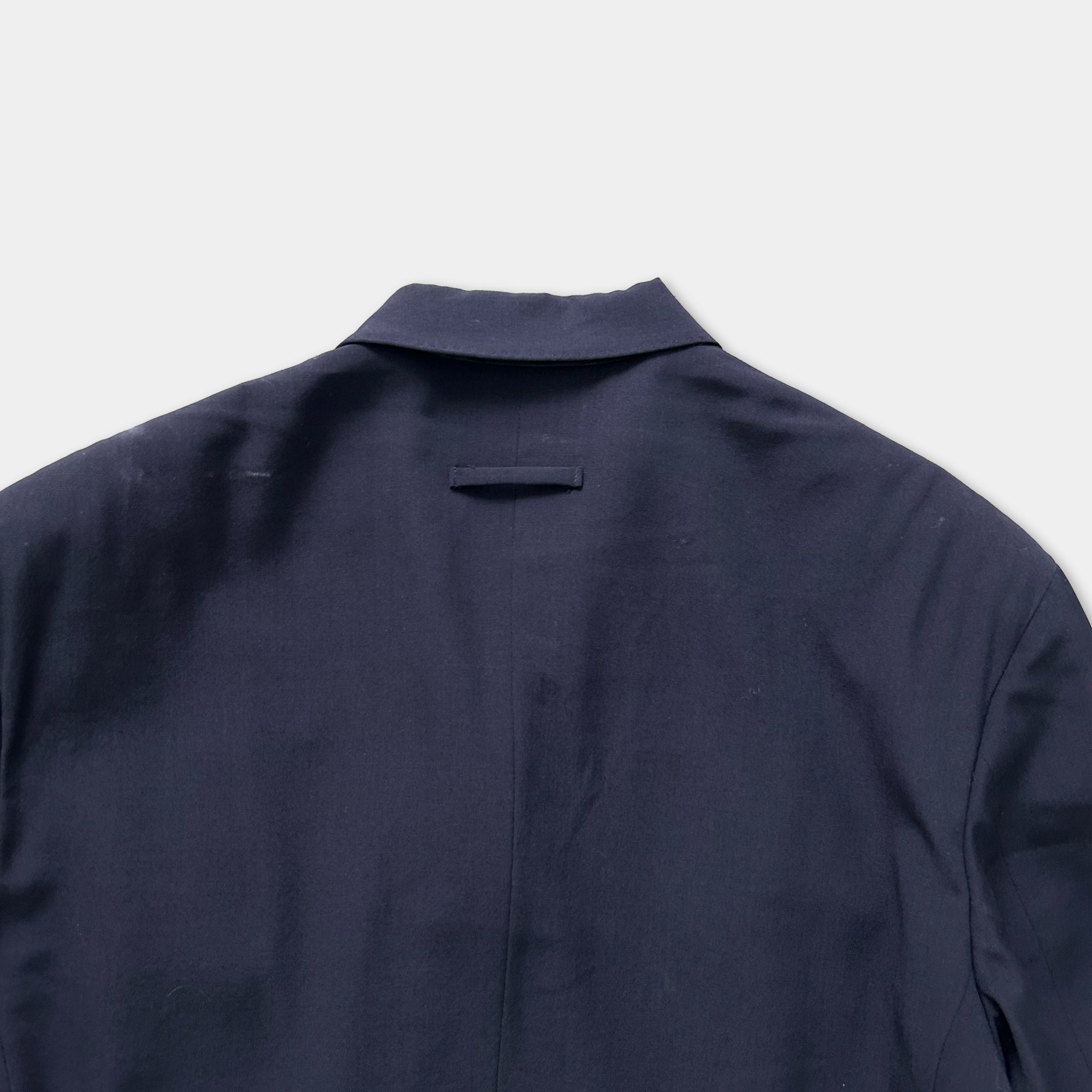 the back of a navy blue jacket or blazer, with a collar and a pocket visible.