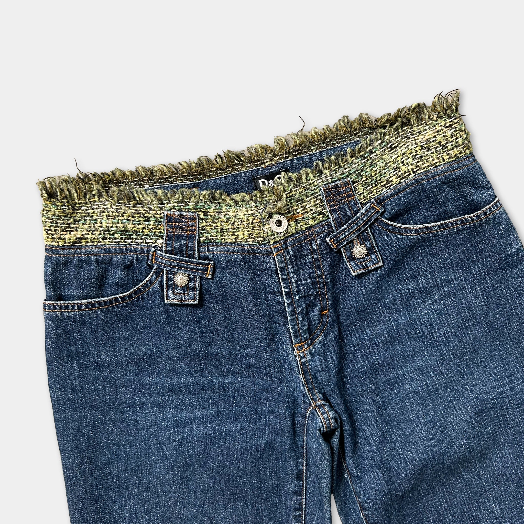 A pair of blue jeans with a fringed waistband and two button closures.