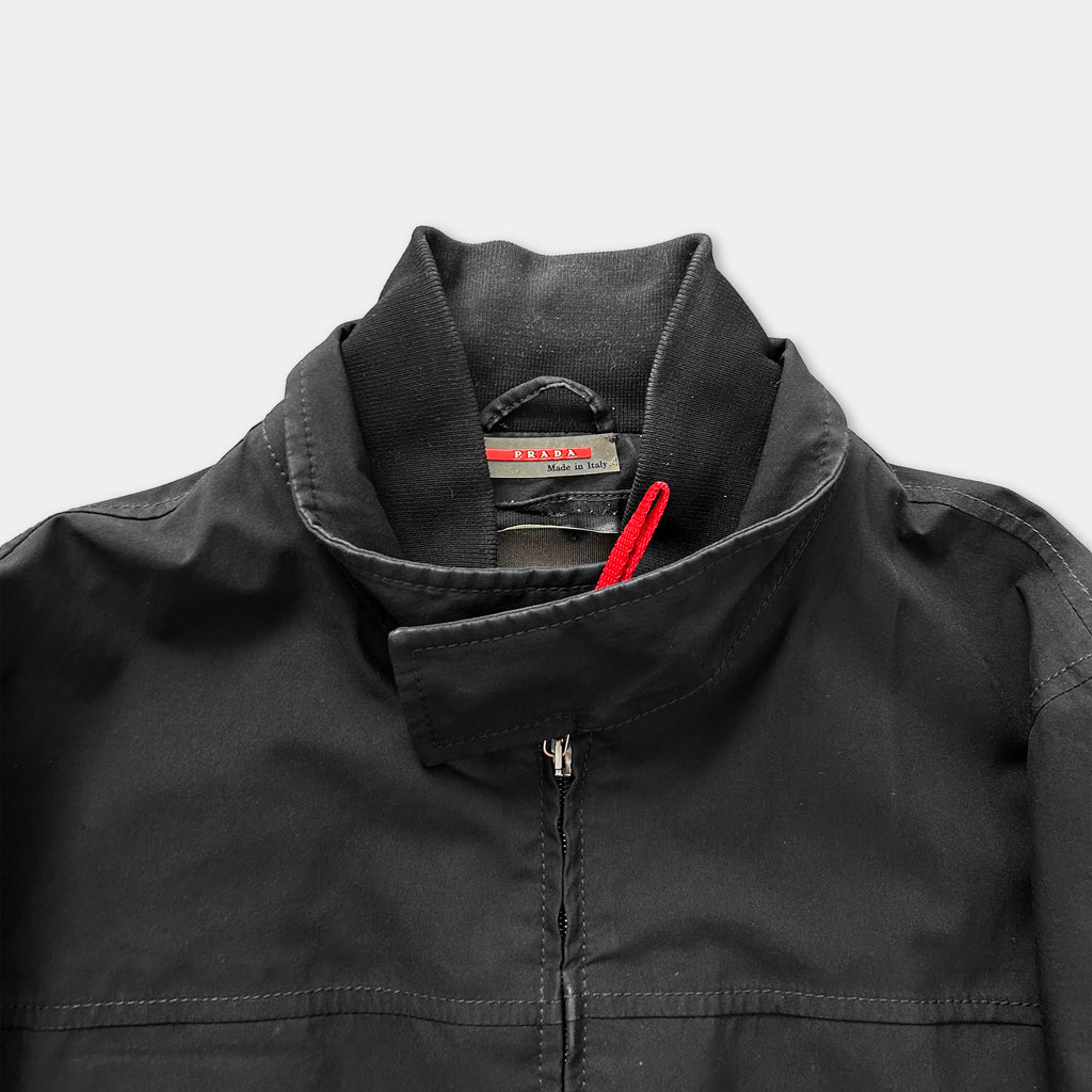 A close-up view of a black jacket with a red zipper pull, showing the collar and zipper.