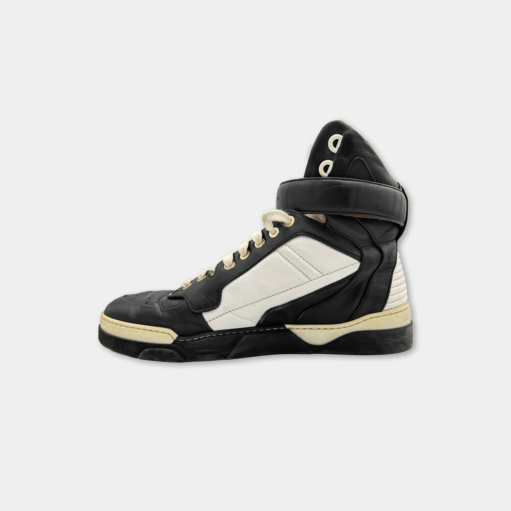 A black and white high-top sneaker with a distinctive design and a black strap.