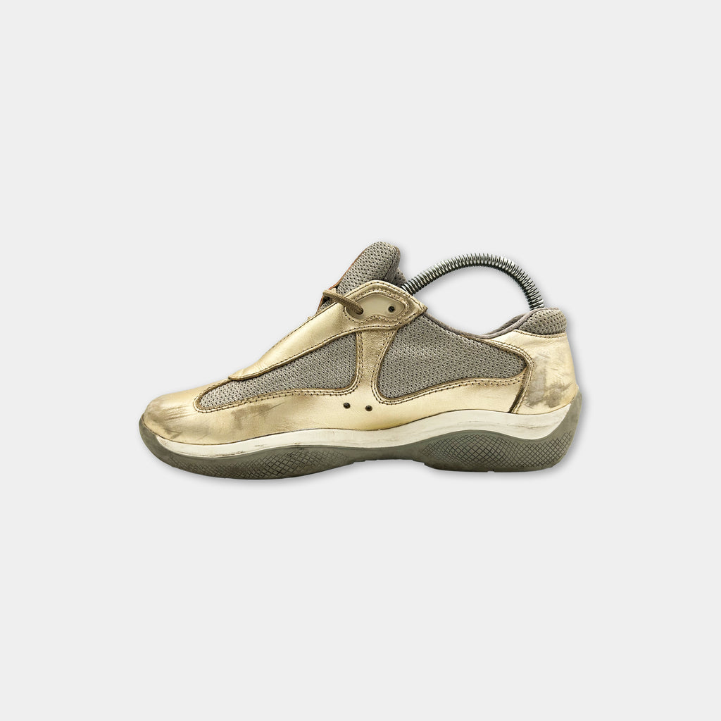 A single, gold-colored sneaker is shown against a plain white background.