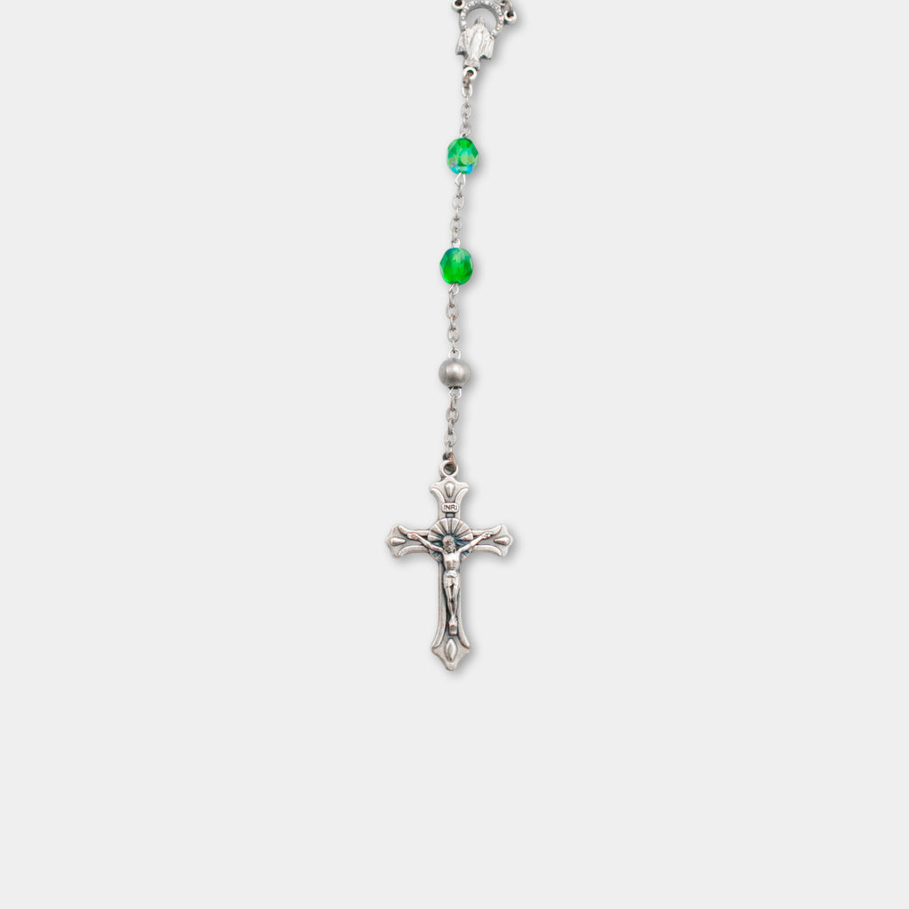 A silver cross with green gemstones hanging from it.