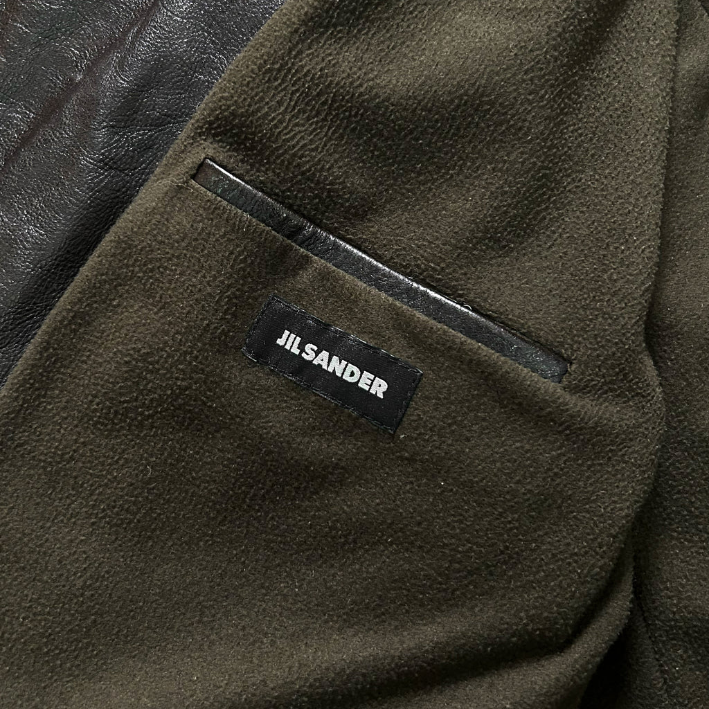A close-up view of a dark green fabric with a label that reads "JIL sander" on it.