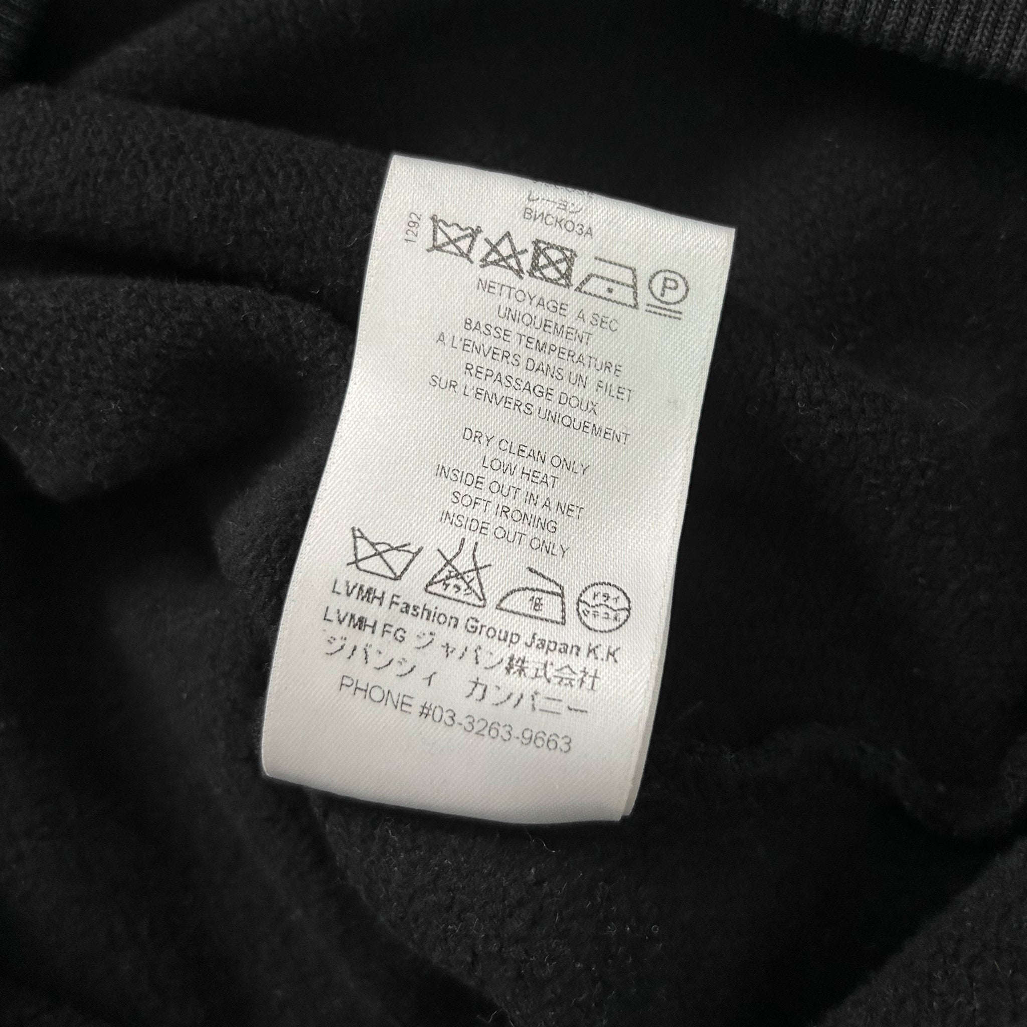 a close-up view of a black fabric with a white label attached to it, which contains text and symbols related to washing instructions and care.
