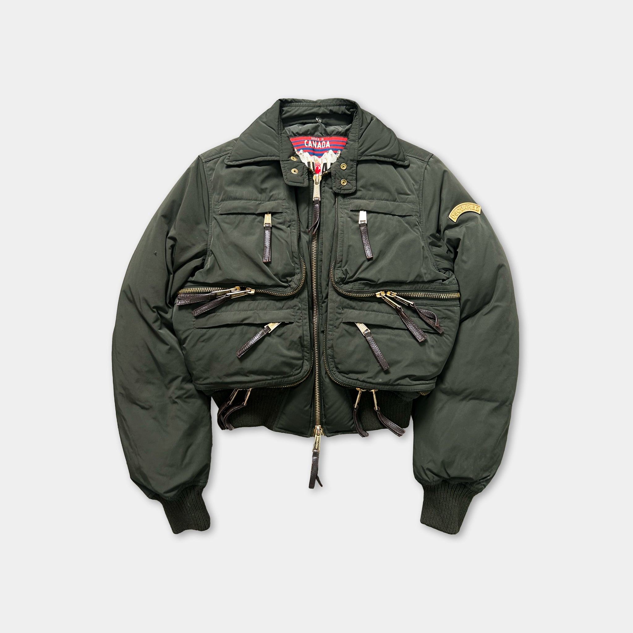 A dark green puffy jacket with multiple zippers and pockets, displayed against a white background.