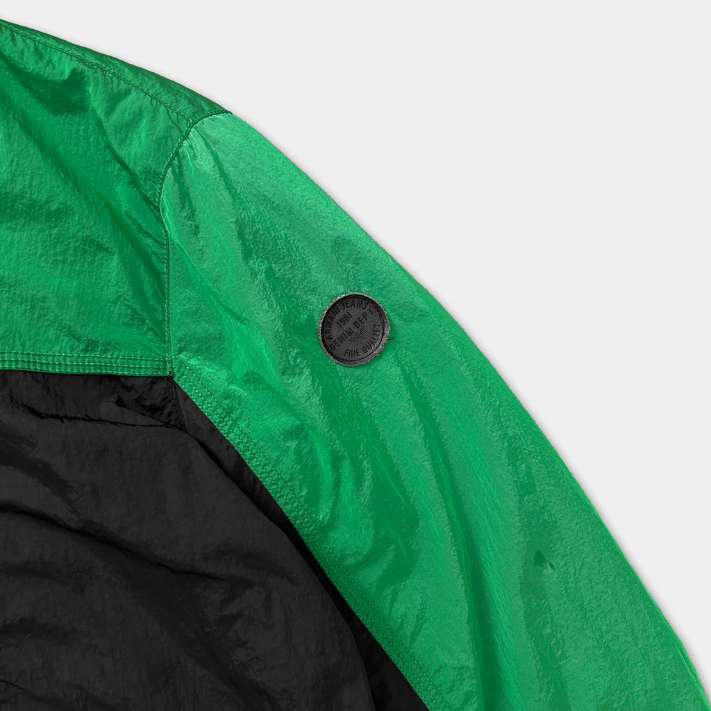 A close-up view of a green and black jacket sleeve, with a small black circular patch on the sleeve.