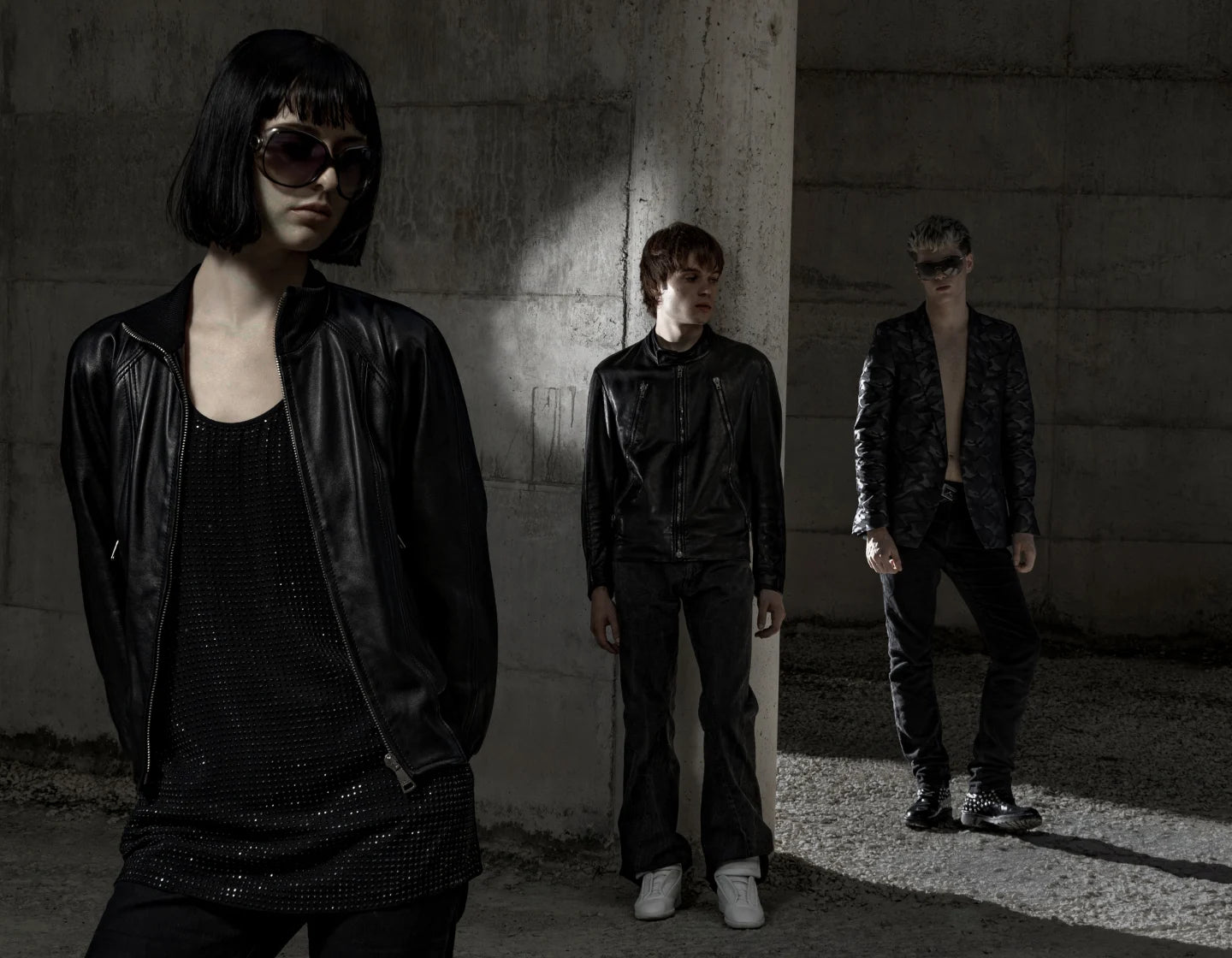 A images of a person wearing a black leather jacket against a concrete wall.